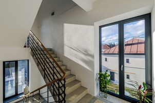 Una escalera con barandilla de madera y puertas de cristal que dan a un espacio exterior con vistas a edificios.