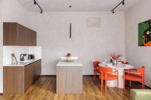 Uma cozinha moderna com armário de madeira, bancada branca e área de refeições com mesa redonda e cadeiras laranjas.