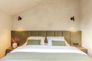 A bedroom with a bed, nightstands, a vase with branches, and two wall-mounted light fixtures.