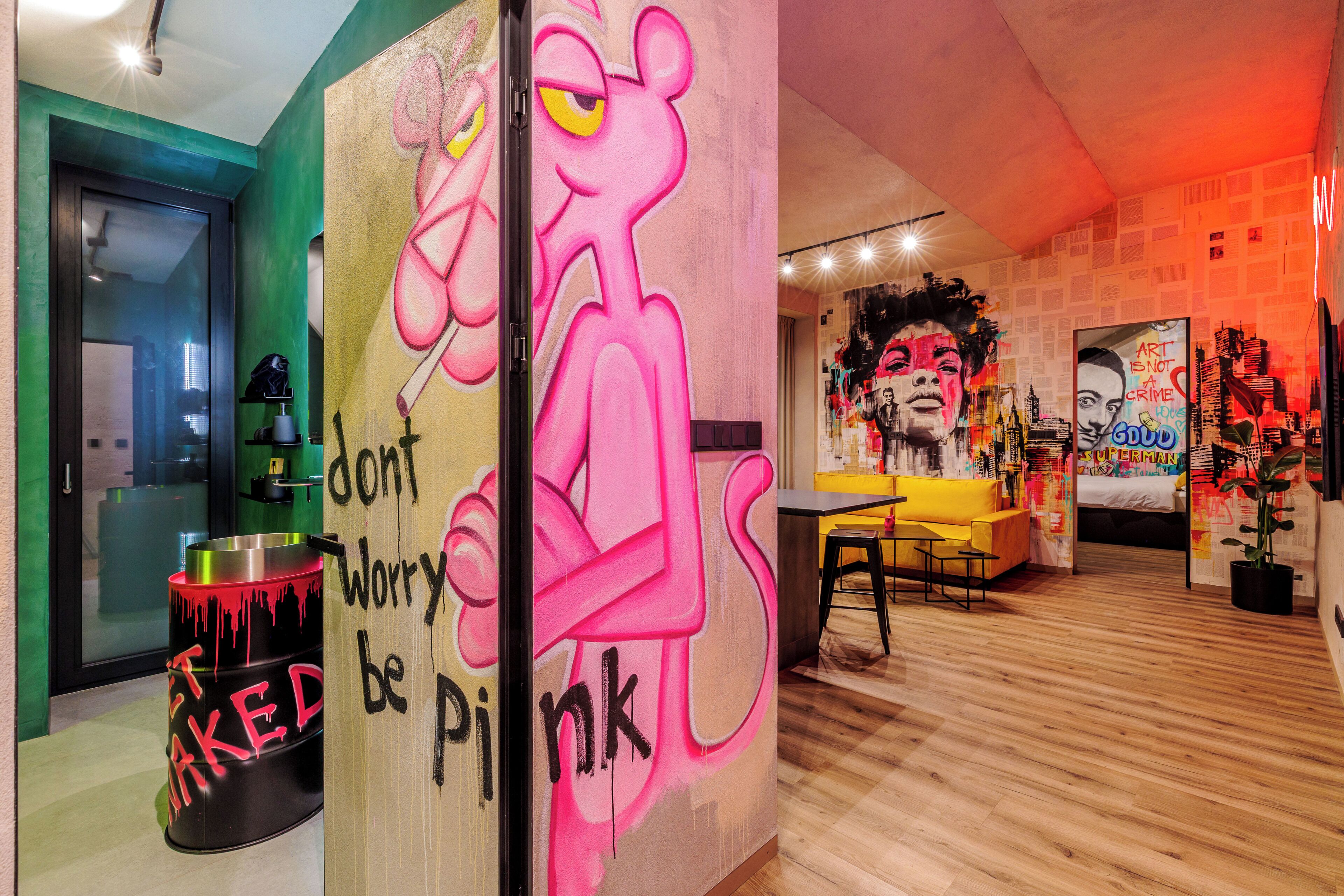 Een kamer met een levendige muurschildering, een houten vloer en een gele bank.
