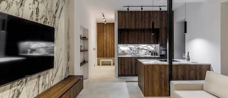 A modern living room with a large flat-screen TV, wooden cabinets, a marble backsplash, and a minimalist sofa.