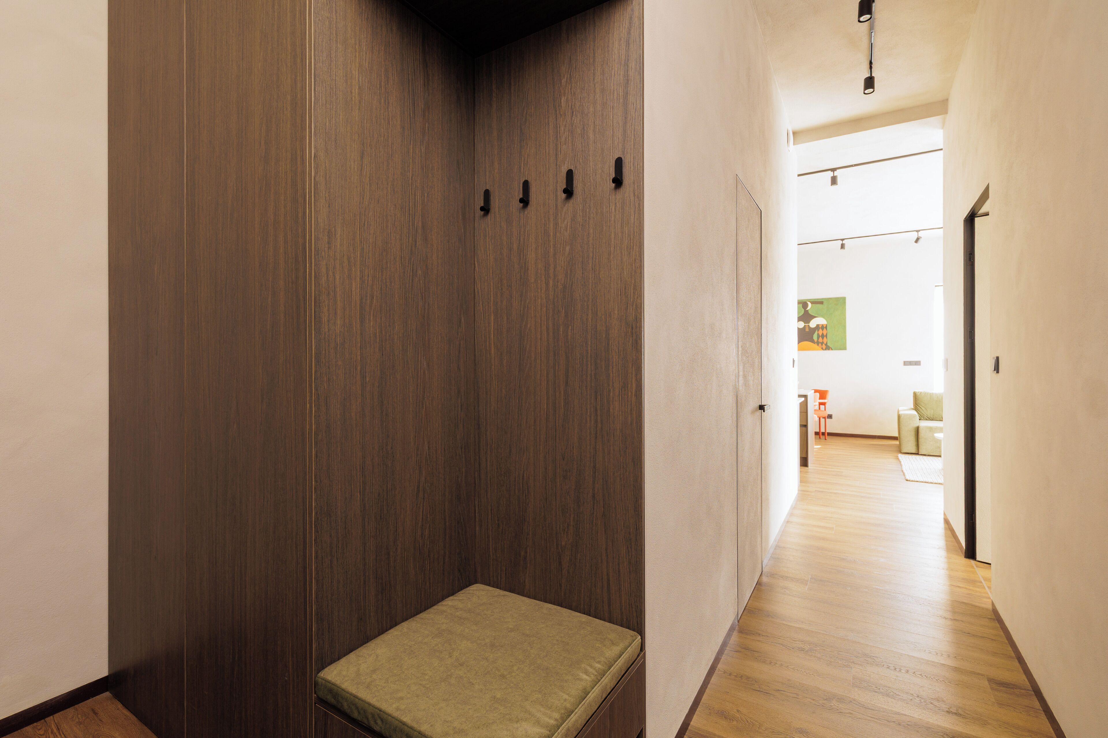 Un pasillo con un banco, paredes de madera y una puerta que da a una habitación con una silla y una mesa.