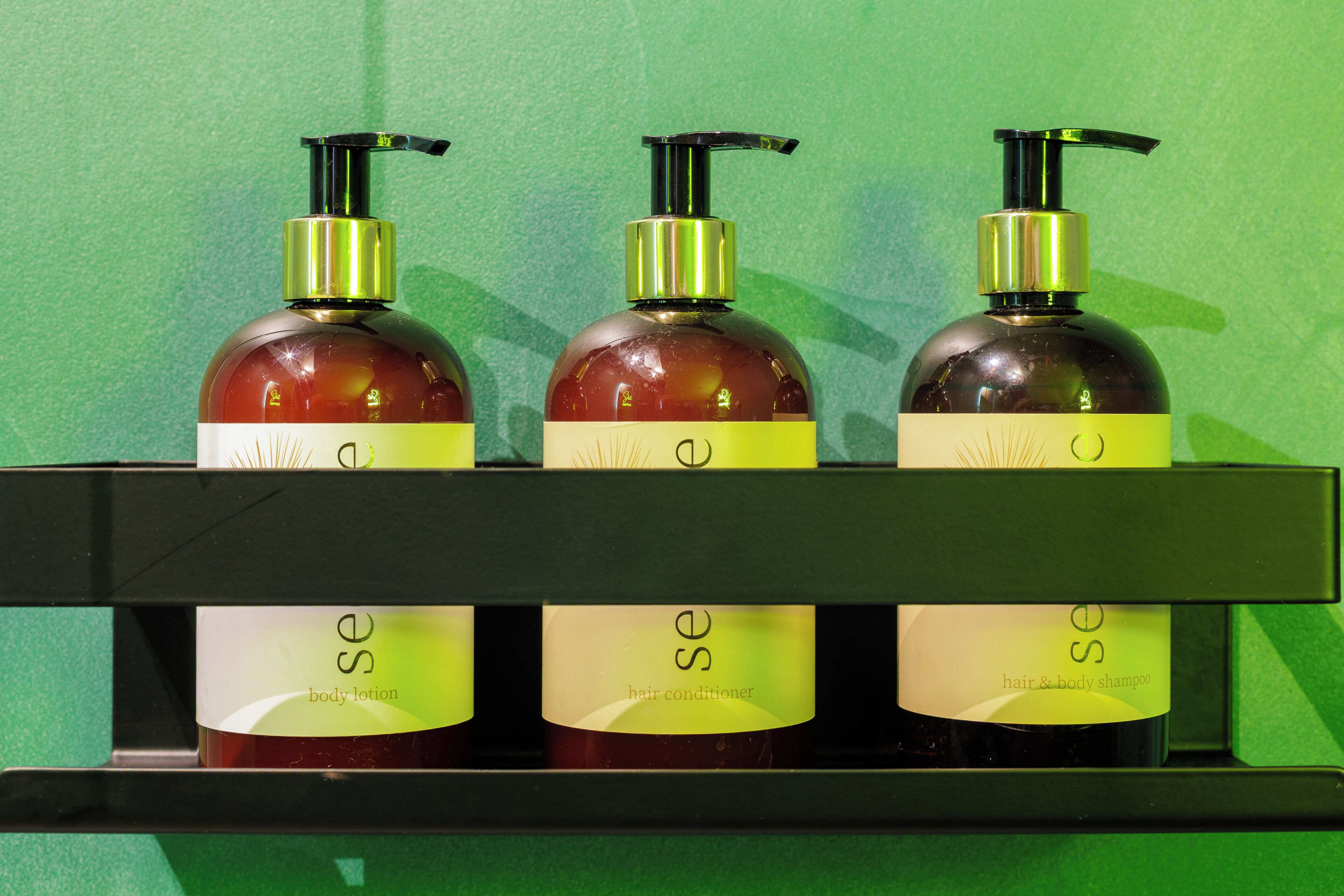 Tres botellas de loción corporal Se, acondicionador para el cabello y champú para cabello y cuerpo sobre una estantería.
