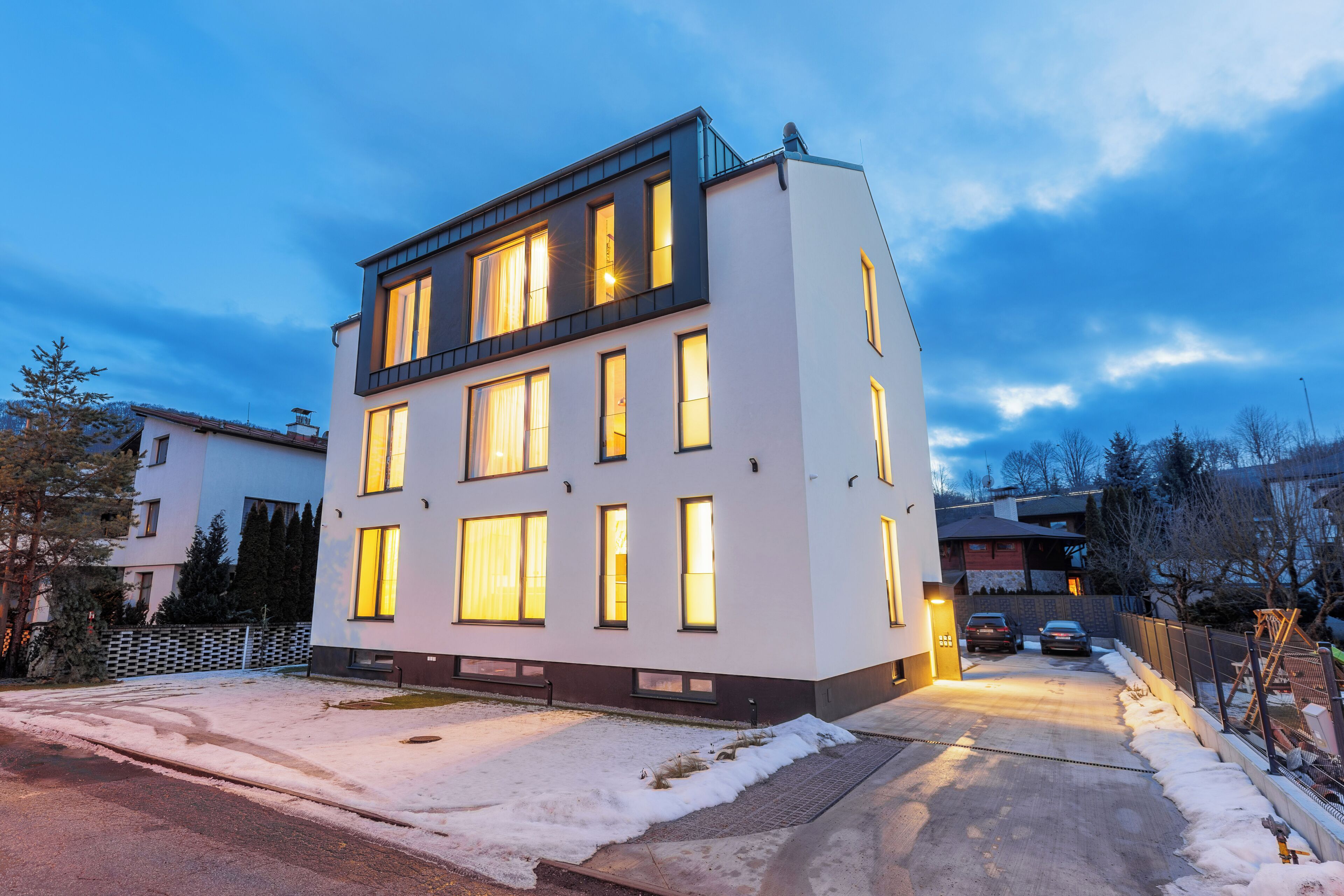 Un edificio moderno de varios pisos con ventanas iluminadas, suelo cubierto de nieve y cielo despejado.