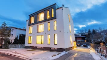 Un edificio moderno de varios pisos con ventanas iluminadas, suelo cubierto de nieve y cielo despejado.