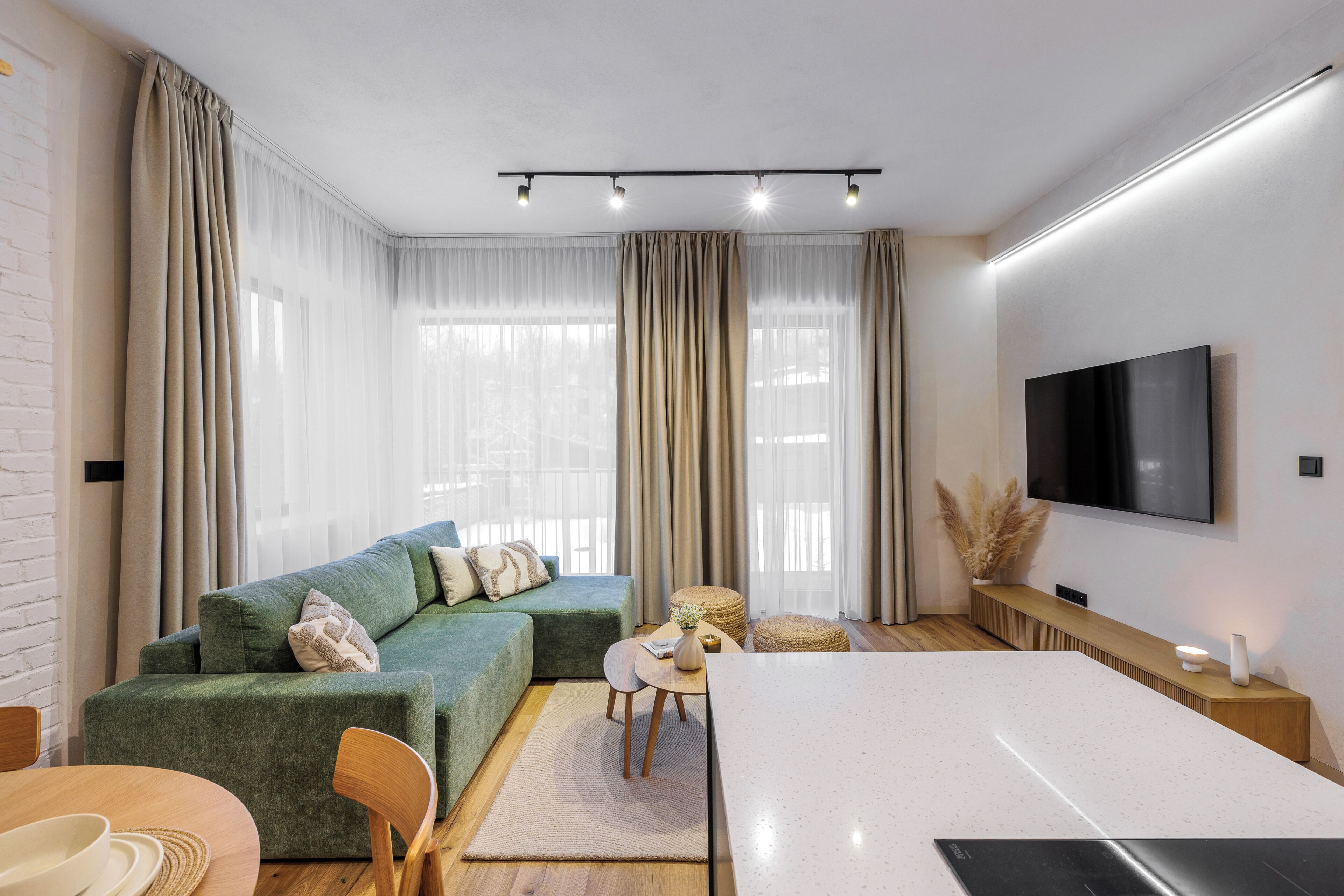 Ein modernes Wohnzimmer mit einem grünen Sofa, einem Esstisch und einem flachbildfernseher an der Wand.
