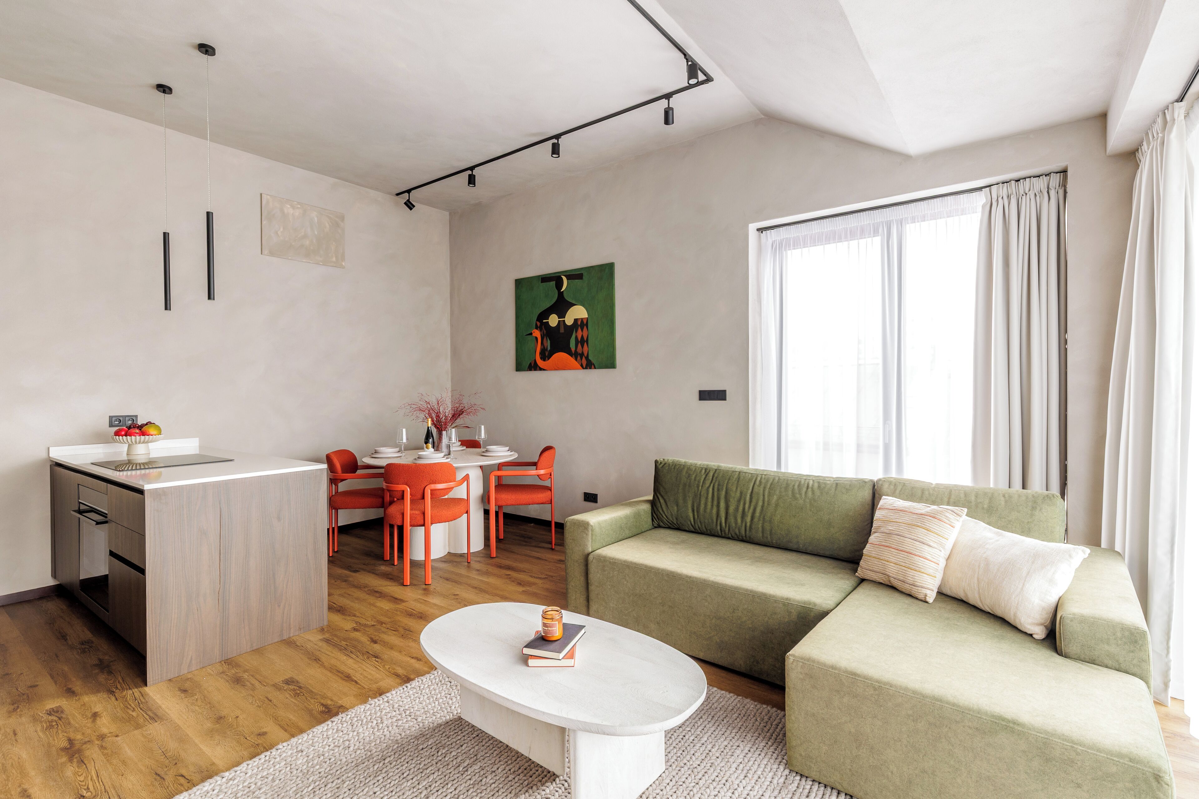 A modern living room with a green sofa, a white coffee table, and a dining area with orange chairs.