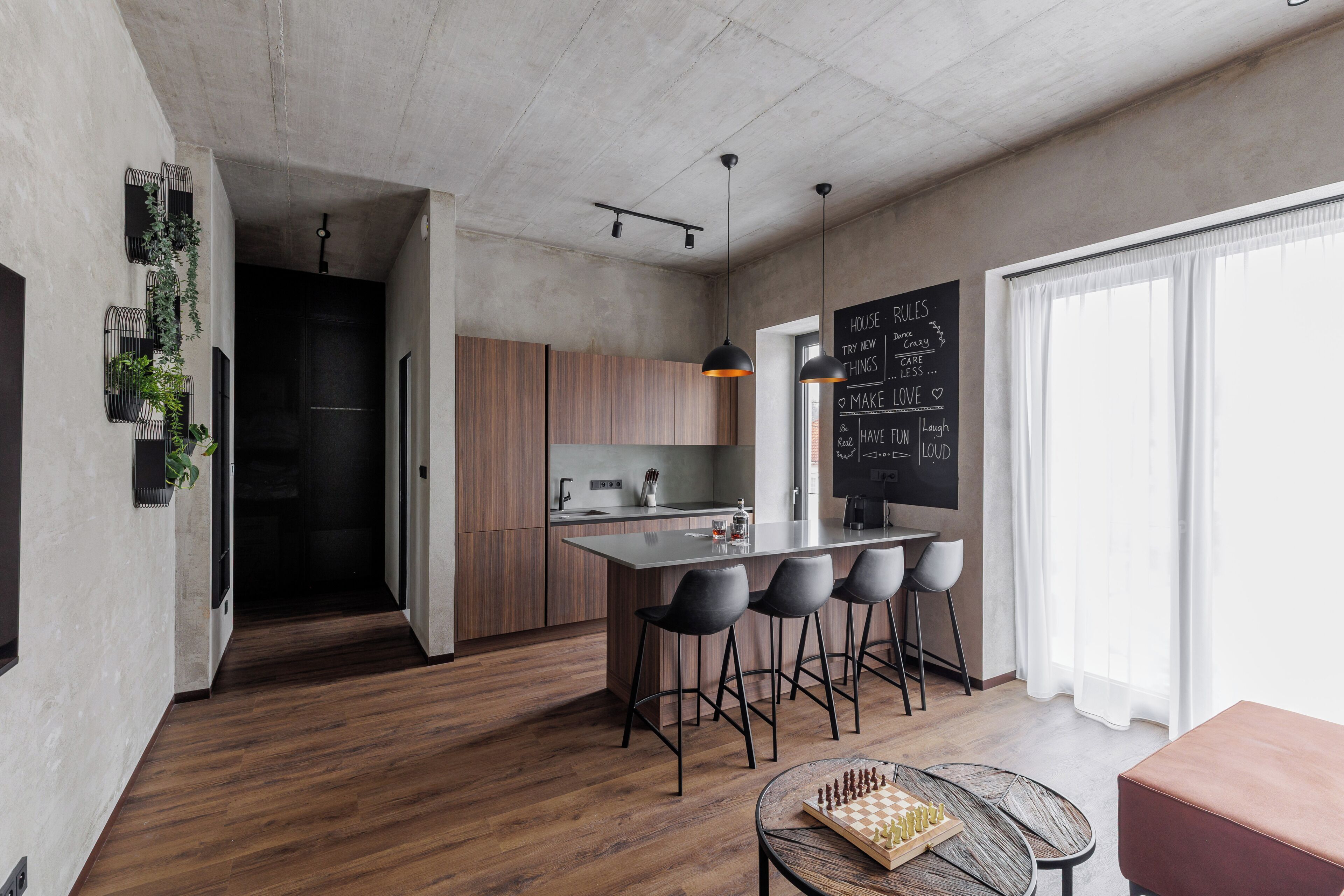 Una cocina moderna con una isla central, taburetes de bar, una pizarra con mensajes motivacionales y un tablero de ajedrez sobre una mesa.