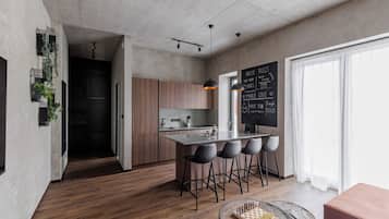 Una cocina moderna con una isla central, taburetes de bar, una pizarra con mensajes motivacionales y un tablero de ajedrez sobre una mesa.