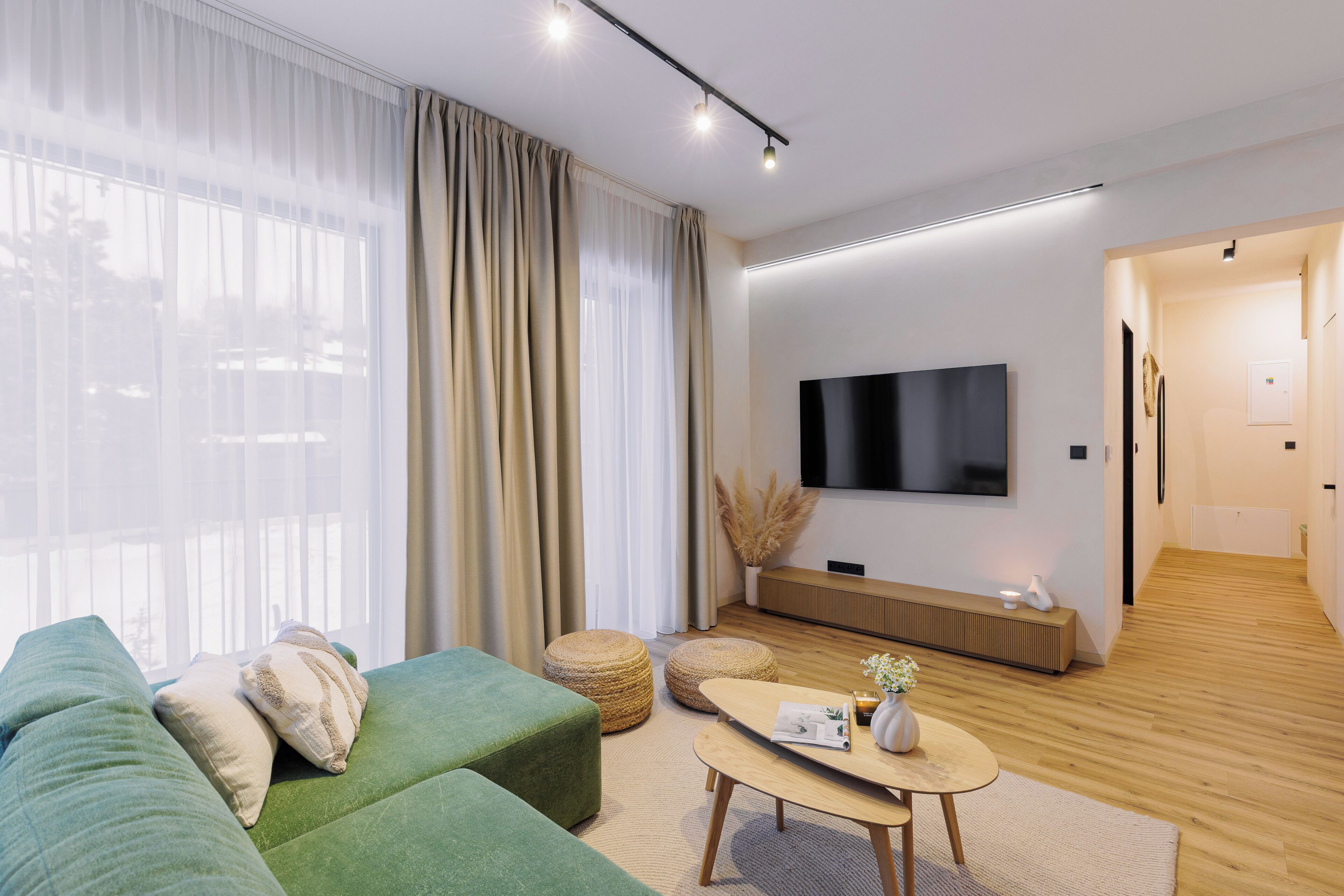 Una sala de estar moderna con un sofá verde, una mesita de centro y un televisor de pantalla plana montado en la pared.