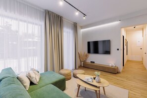 A modern living room with a green sofa, a coffee table, and a flat-screen TV mounted on the wall.