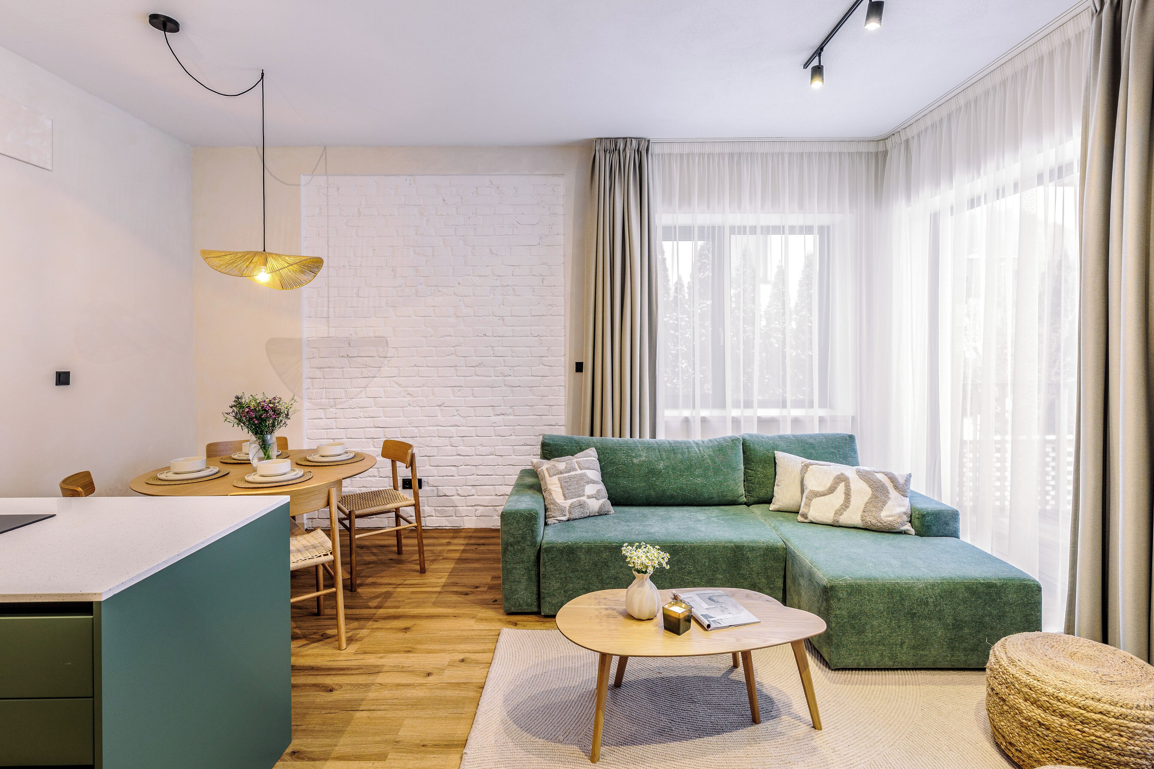 A modern living room with a green sofa, a round coffee table, a dining area with a white table, and a kitchen area.