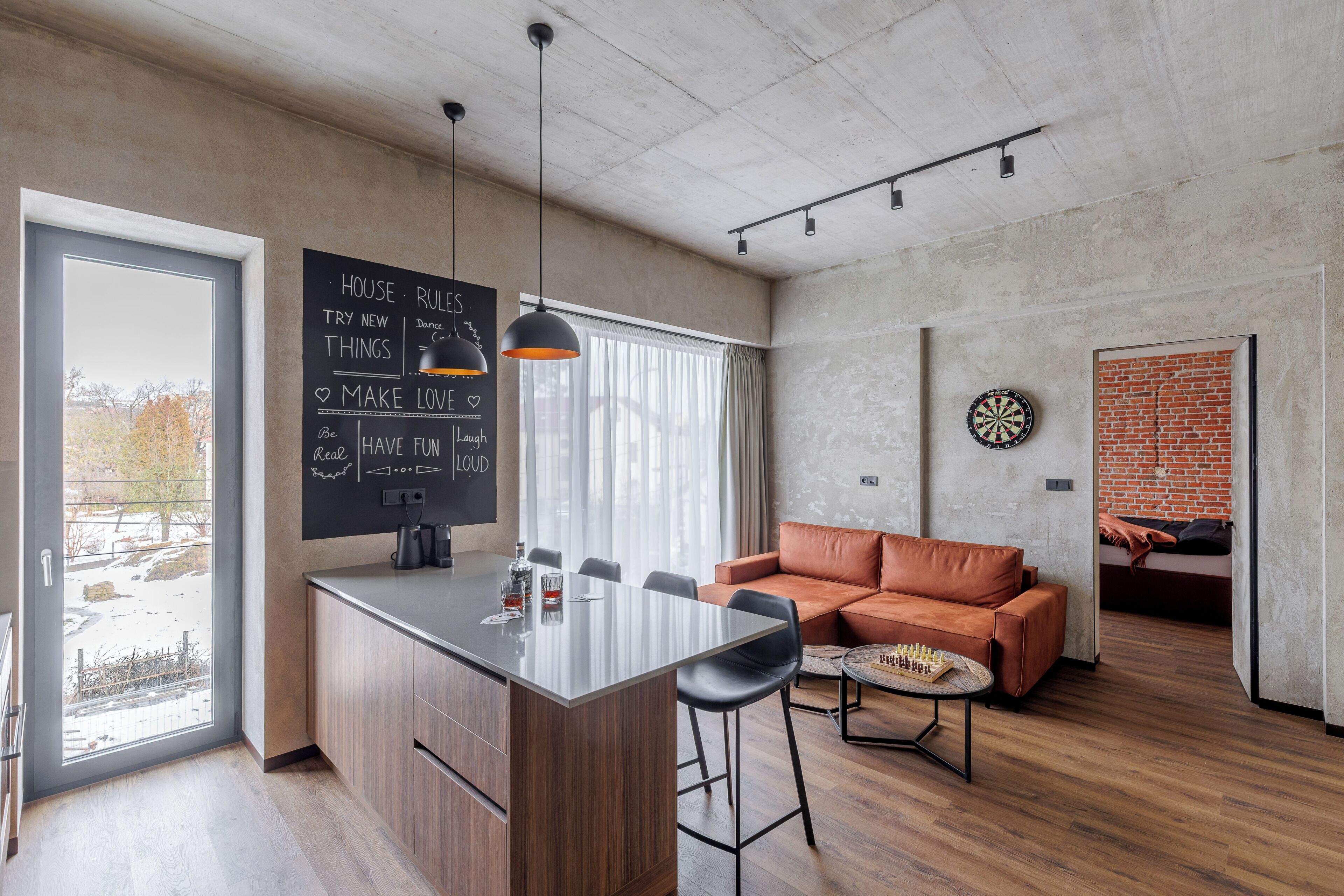 A modern kitchen with a central island, a dining area with a leather sofa, and a dartboard on the wall.