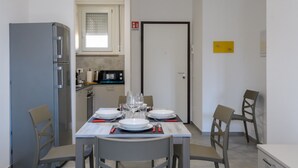 A dining area with a table set for four, a kitchen with a refrigerator and stove, and a door with a fire alarm. - A bright and practical 60 square meters apartment, perfect for two people, located on the second floor of a building with an elevator (NOT accessible to people with disabilities).The property is situated in a quiet area and is ideally located for those w (Marotta)