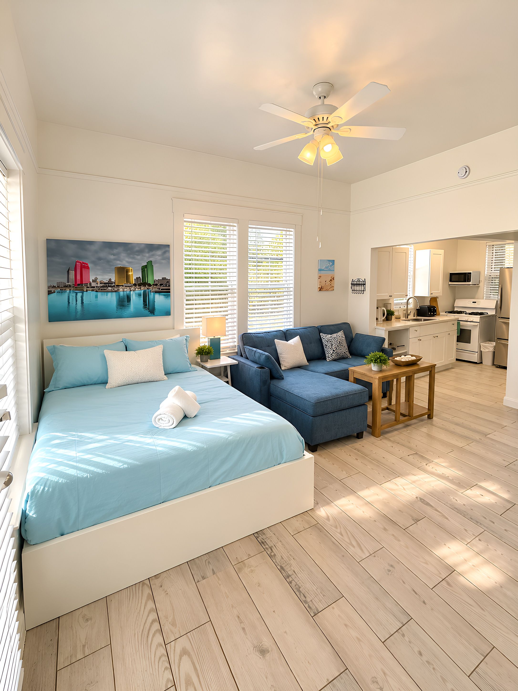 A bedroom with a bed, a blue sofa, a ceiling fan, and a view of the kitchen.
