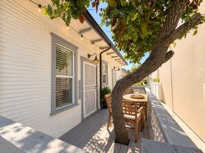 A white building with a covered patio area, a wooden table with chairs, and string lights. - Stylish Studio w Patio Walk Downtown & Balboa Park (San Diego)