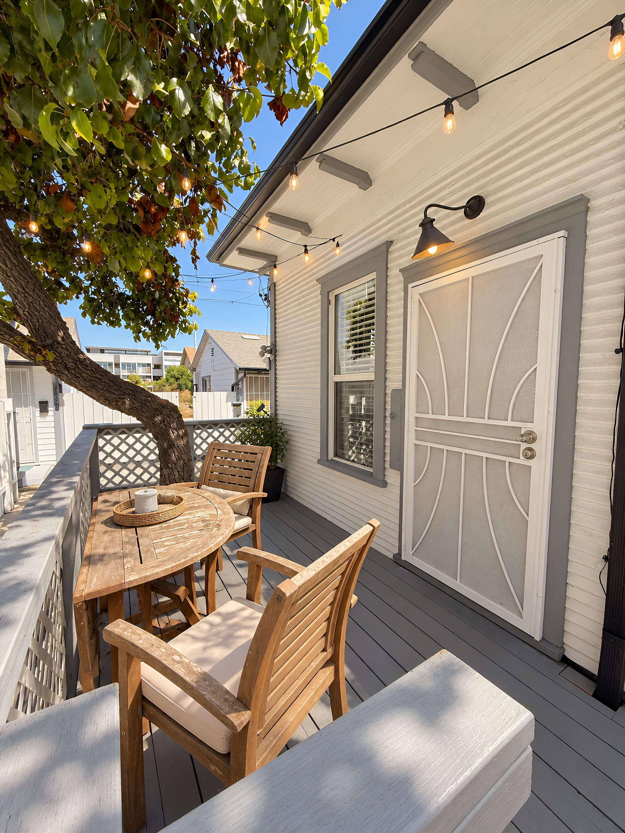 A wooden deck with a table and chairs, a white door with a decorative design, and string lights.