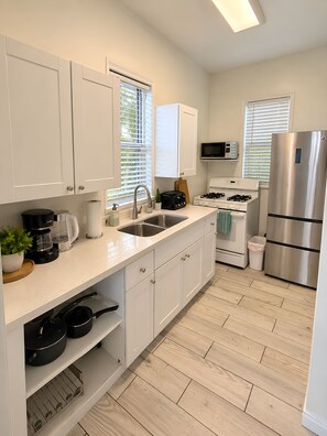 A modern kitchen with white cabinetry, stainless steel appliances, and a wooden floor. - Stylish Studio w Patio Walk Downtown & Balboa Park (San Diego)