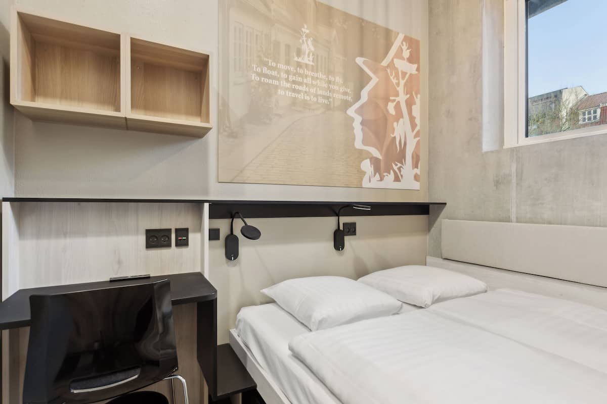 A modern hotel room with a bed, a desk, and a wall-mounted artwork.