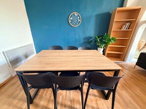 Ein Essbereich mit einem Holztisch, vier schwarzen Stühlen, einer blauen Wand, einem dekorativen Teller, einem Bücherregal und einer Topfpflanze.