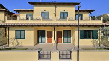 A two-story building with a flat roof, green shutters, and a balcony on the upper floor.