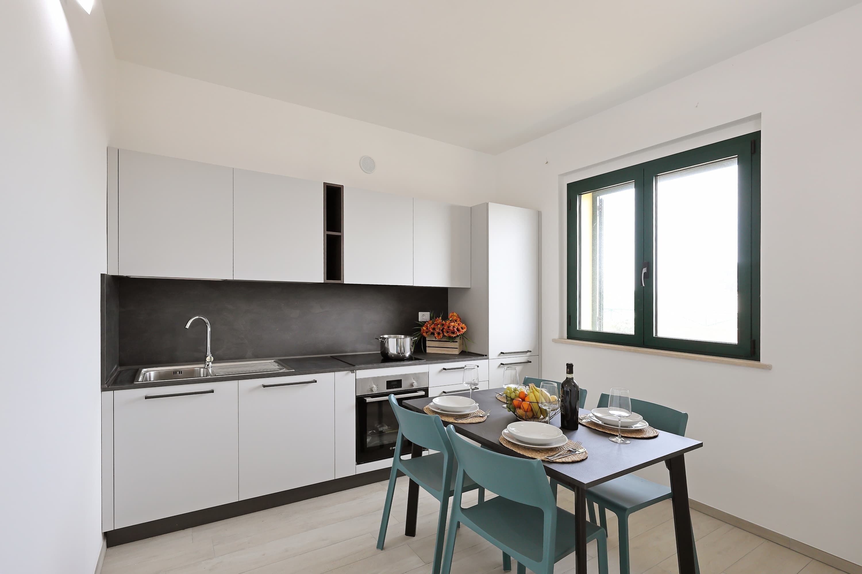 Uma cozinha moderna com armários brancos, bancada preta e um espaço de jantar com mesa posta para dois.