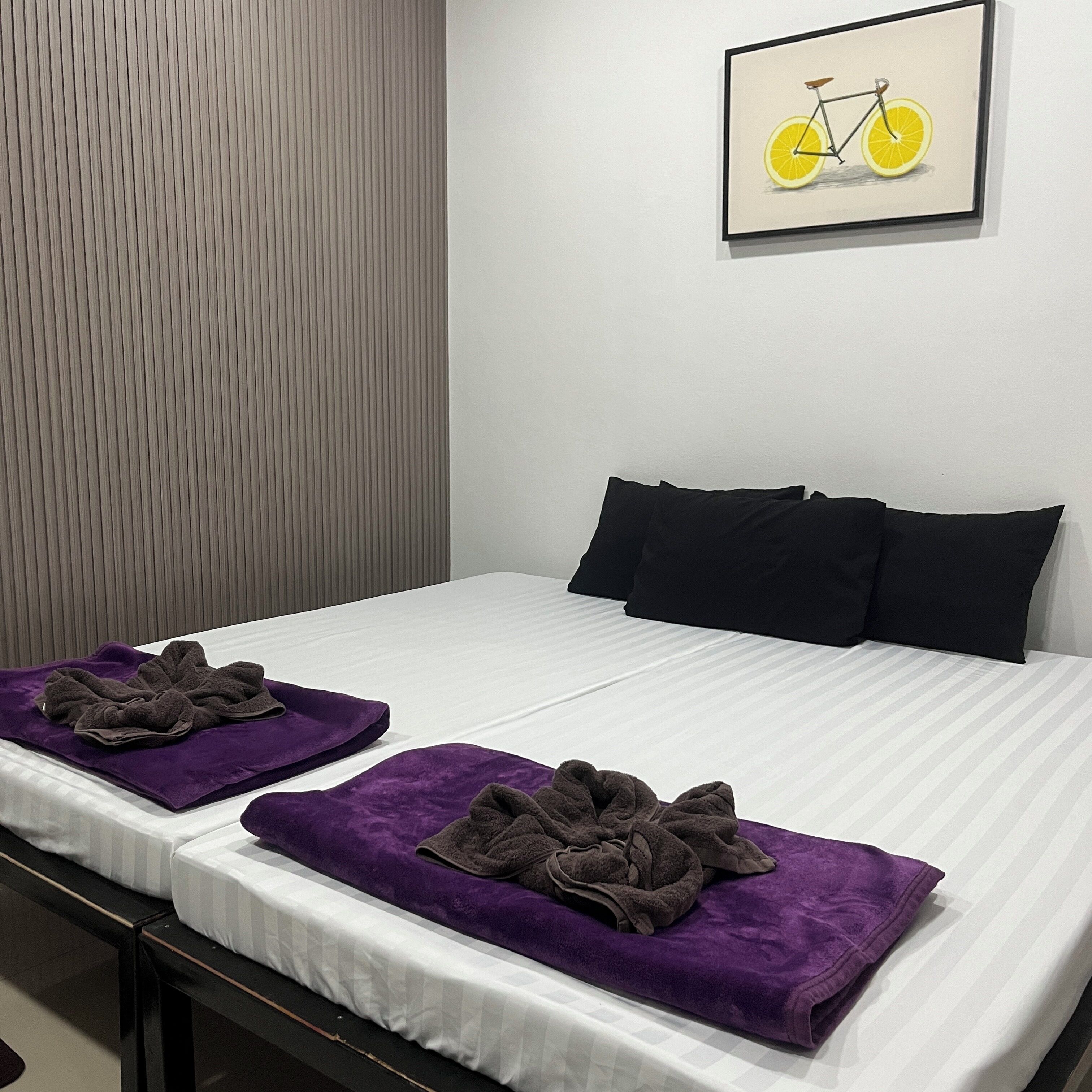 Een hotelkamer met twee bedden, elk voorzien van een paarse handdoek en een zwart kussen.