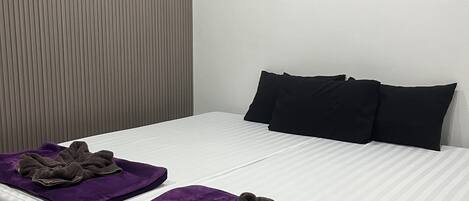 Een hotelkamer met twee bedden, elk voorzien van een paarse handdoek en een zwart kussen.