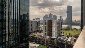 Un edificio de gran altura con fachada de vidrio, un río y el perfil de la ciudad al fondo.
