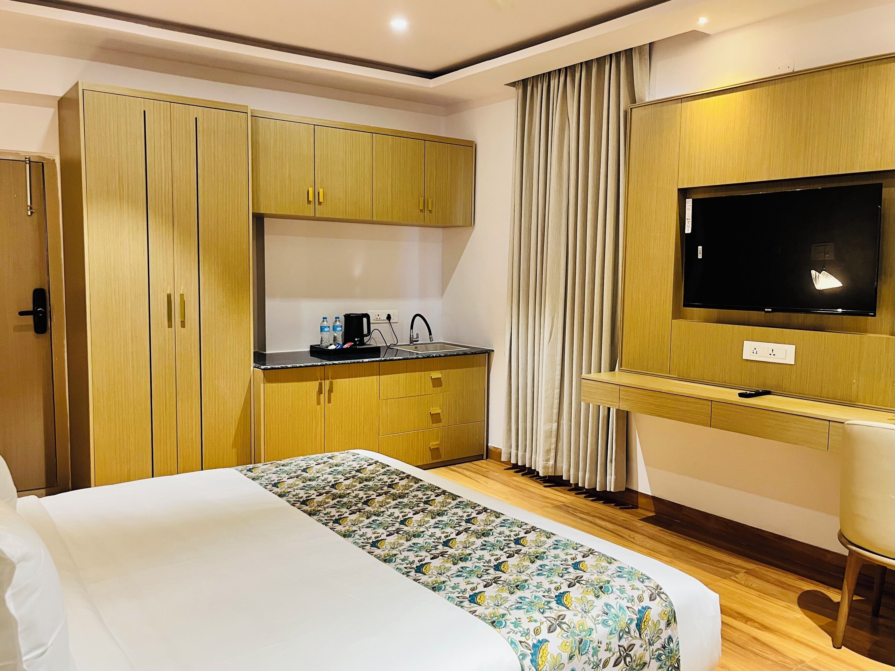 Een hotelkamer met een bed, een televisie, een kleine kitchenette en een raam met gordijnen.