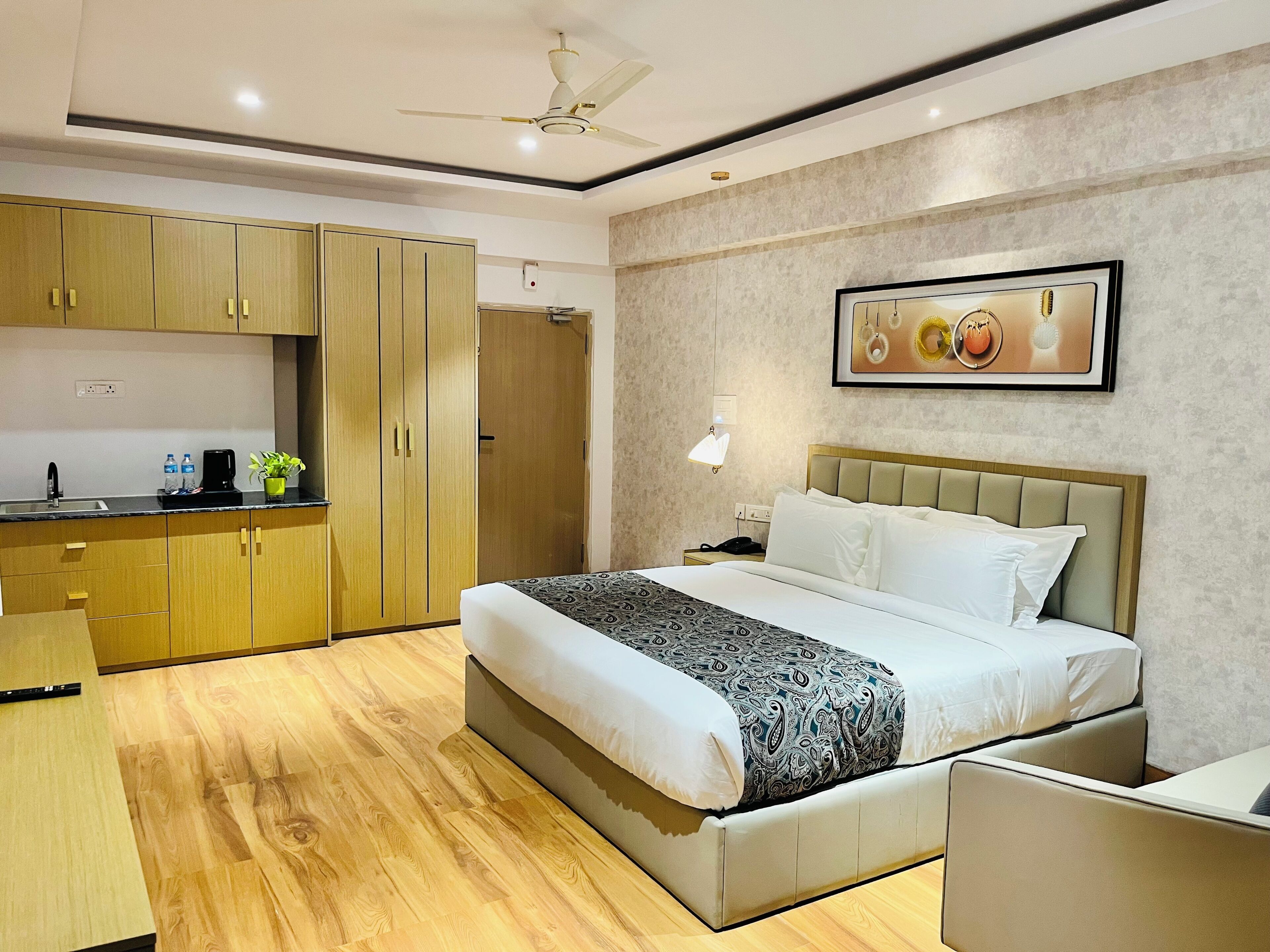 A hotel room with a bed, bedside table, a desk, a wardrobe, and a ceiling fan.