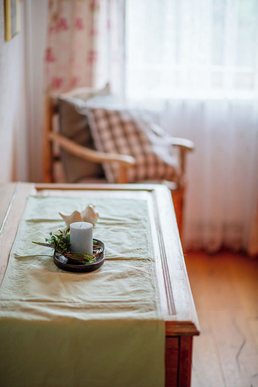 A room with a bed, a bedside table with a candle, and a window with curtains.