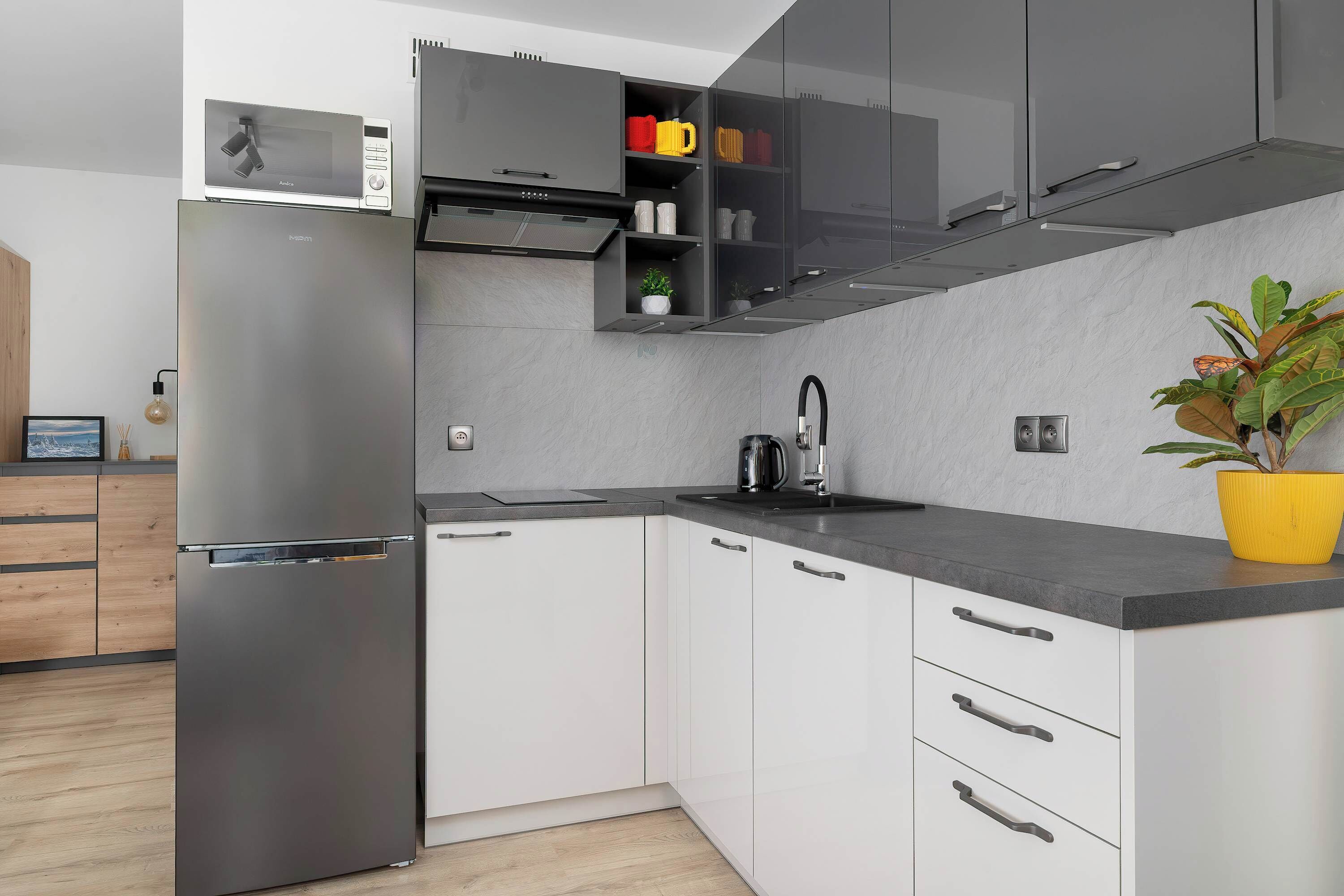 Cocina moderna con refrigerador de acero inoxidable, microondas, pileta y planta en maceta.