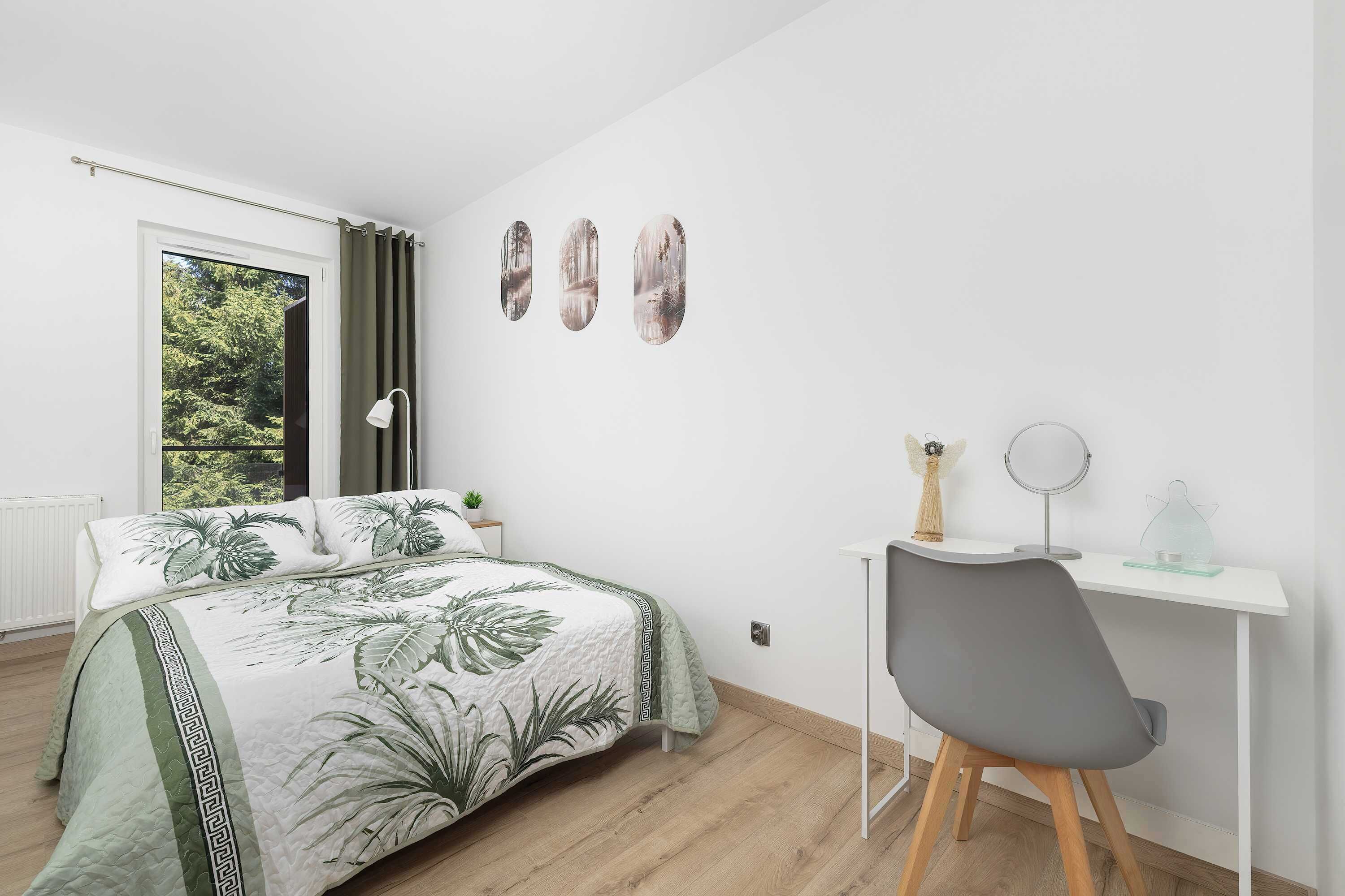 A bedroom with a bed, a desk, a chair, a window, and wall art.