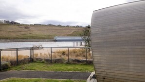 A waterfront view with a large cylindrical building, a picnic table, and a fence.
