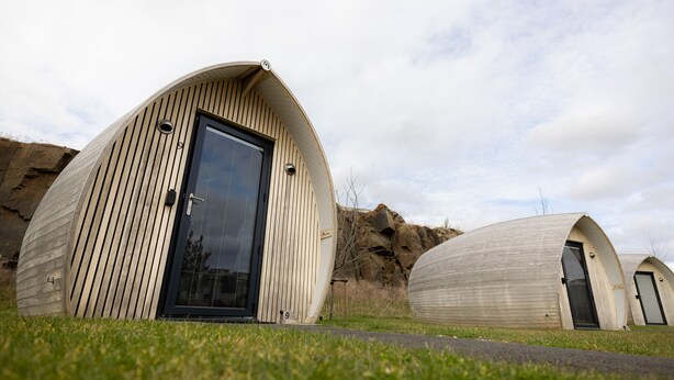 Two dome-shaped structures with a wooden exterior, a door, and a window, set against a natural landscape.