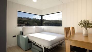 A compact room with a bed, a dining table, and a window offering a view of a landscape.