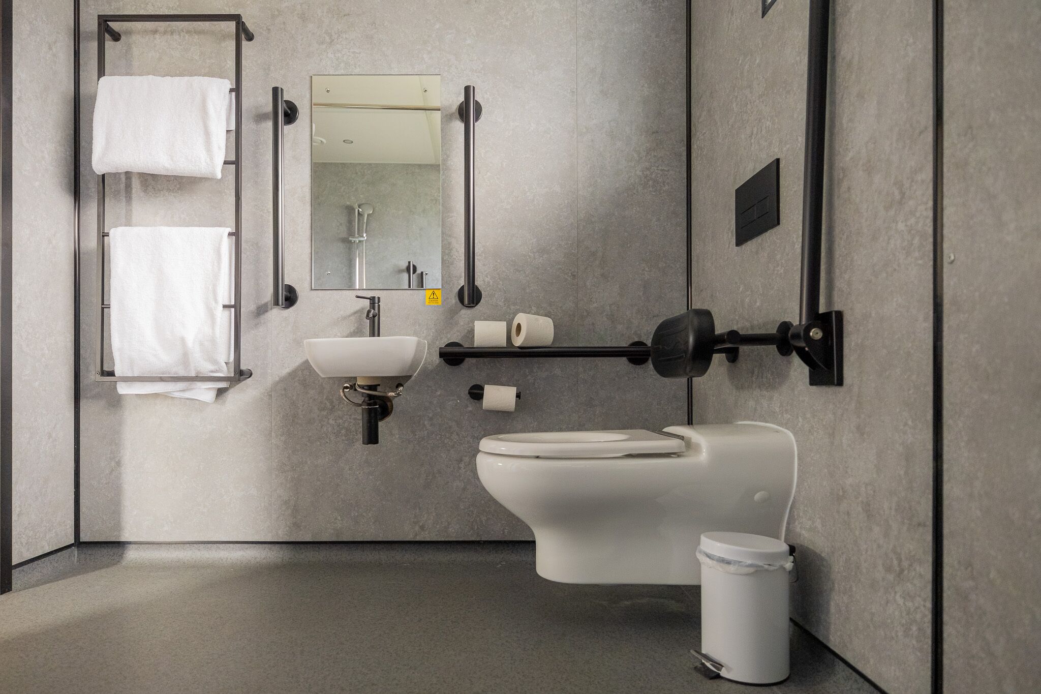 A modern bathroom with a toilet, sink, towel rack, and mirror.