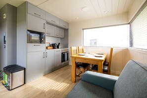 A compact kitchen with a microwave, oven, and sink, a dining table with chairs, and a window with blinds.