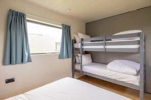 A bunk bed room with a window, curtains, and a power outlet.