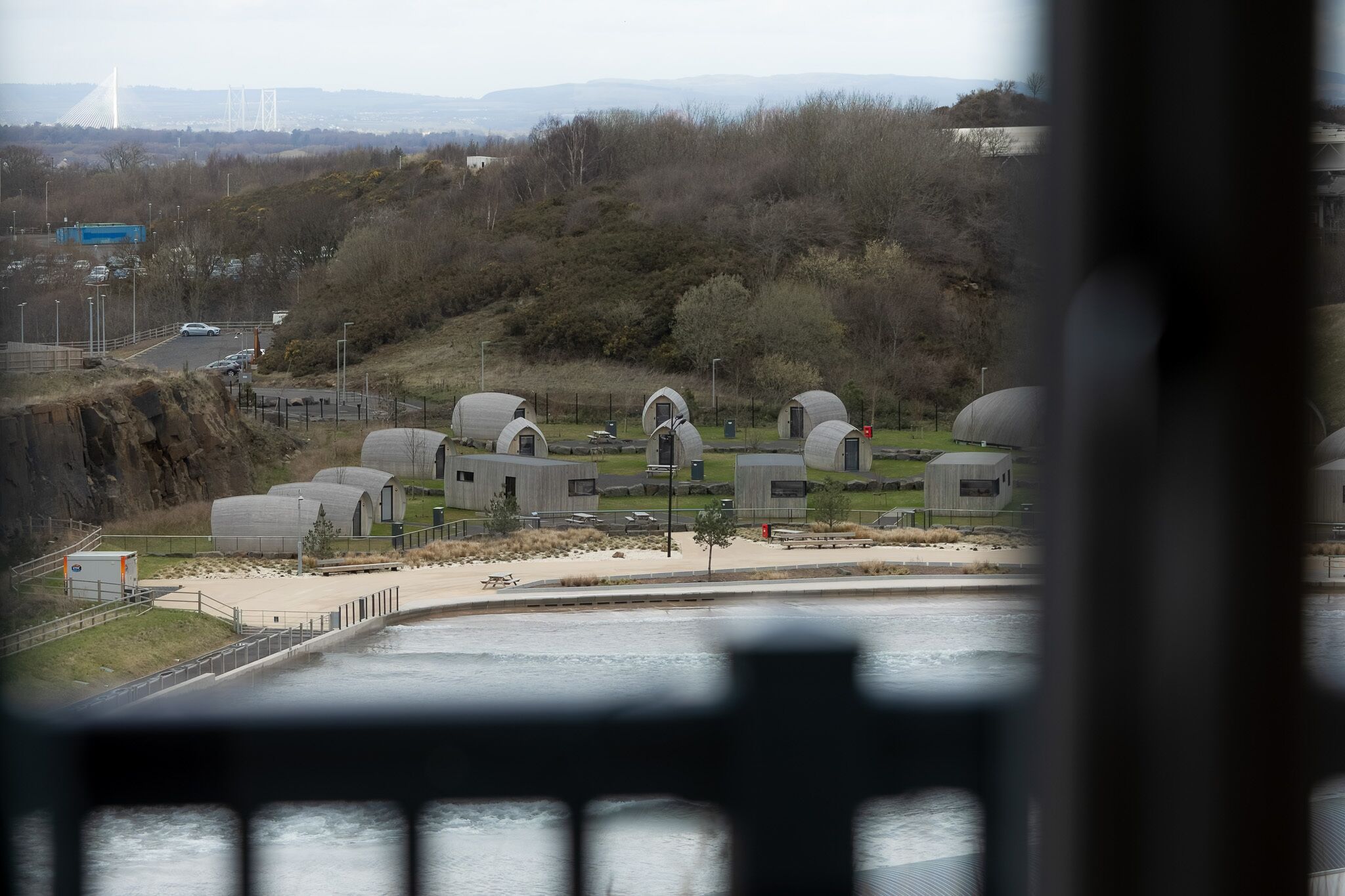 A view of a coastal area with several cylindrical structures, a bridge, and a road in the background.