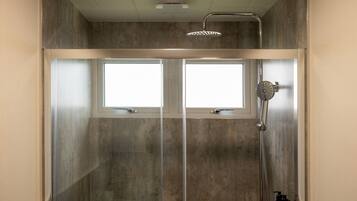 A shower enclosure with a glass door, a handheld showerhead, and a bottle of shampoo.