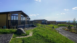 Un bâtiment moderne doté d’une passerelle couverte, d’un espace extérieur aménagé pour s’asseoir et offrant une vue sur les collines lointaines.