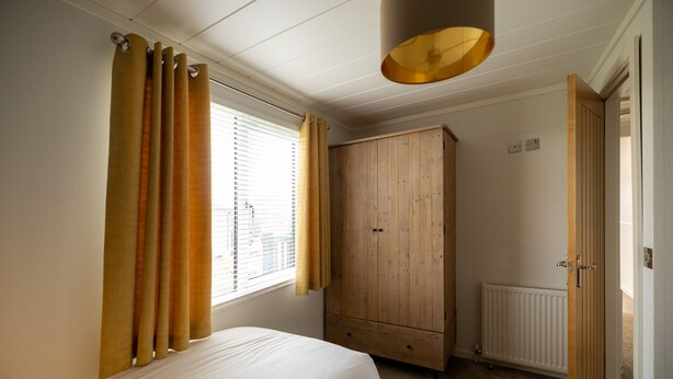 Une chambre à coucher avec un lit, une armoire en bois, un radiateur et une fenêtre avec des rideaux.