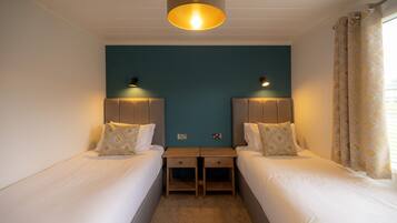A hotel room with two single beds, a small desk, a ceiling light, and a window with curtains.