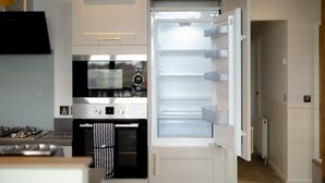 Cocina moderna con horno empotrado, microondas y refrigerador con las puertas abiertas.