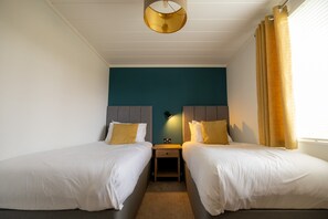 Een hotelkamer met twee bedden, een nachtkastje, een wandlamp en een raam met gordijnen.