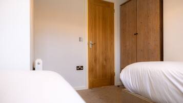 A bedroom with a wooden door, a bed, and a white bedside table.