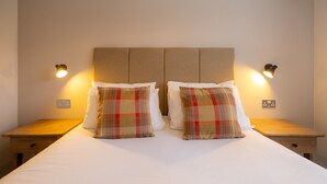 Una cama doble con dos almohadas, cabecera, mesitas de noche e iluminación de pared.