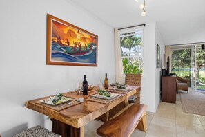 A dining area with a wooden table set for four, a painting above, and a view of greenery outside. - Kuilima Estates | Golf Course View 2 BR, Sleeps 6 | Car Incl. w/ 6+ Nights | ML-4145 by KBM (Kahuku)